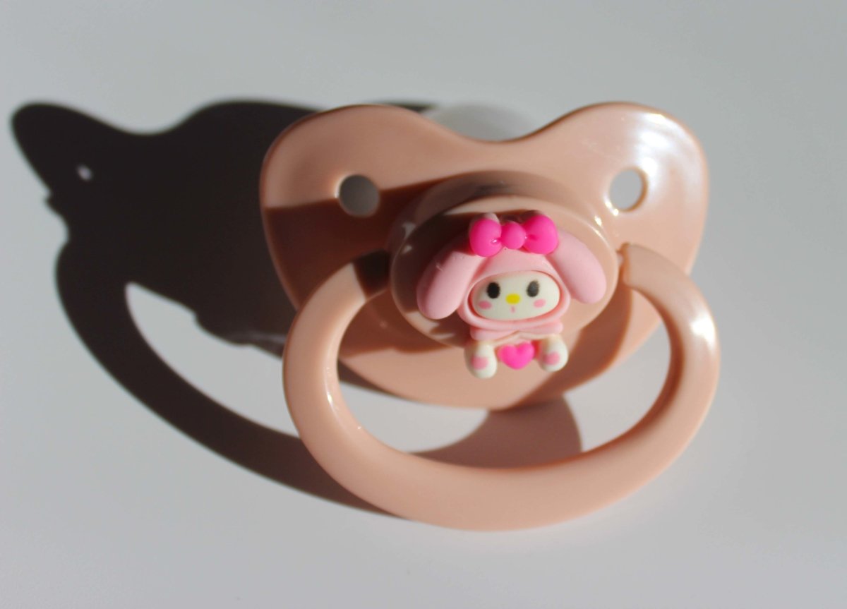 kawaii pink adult pacifier with bunny charm on a white background.