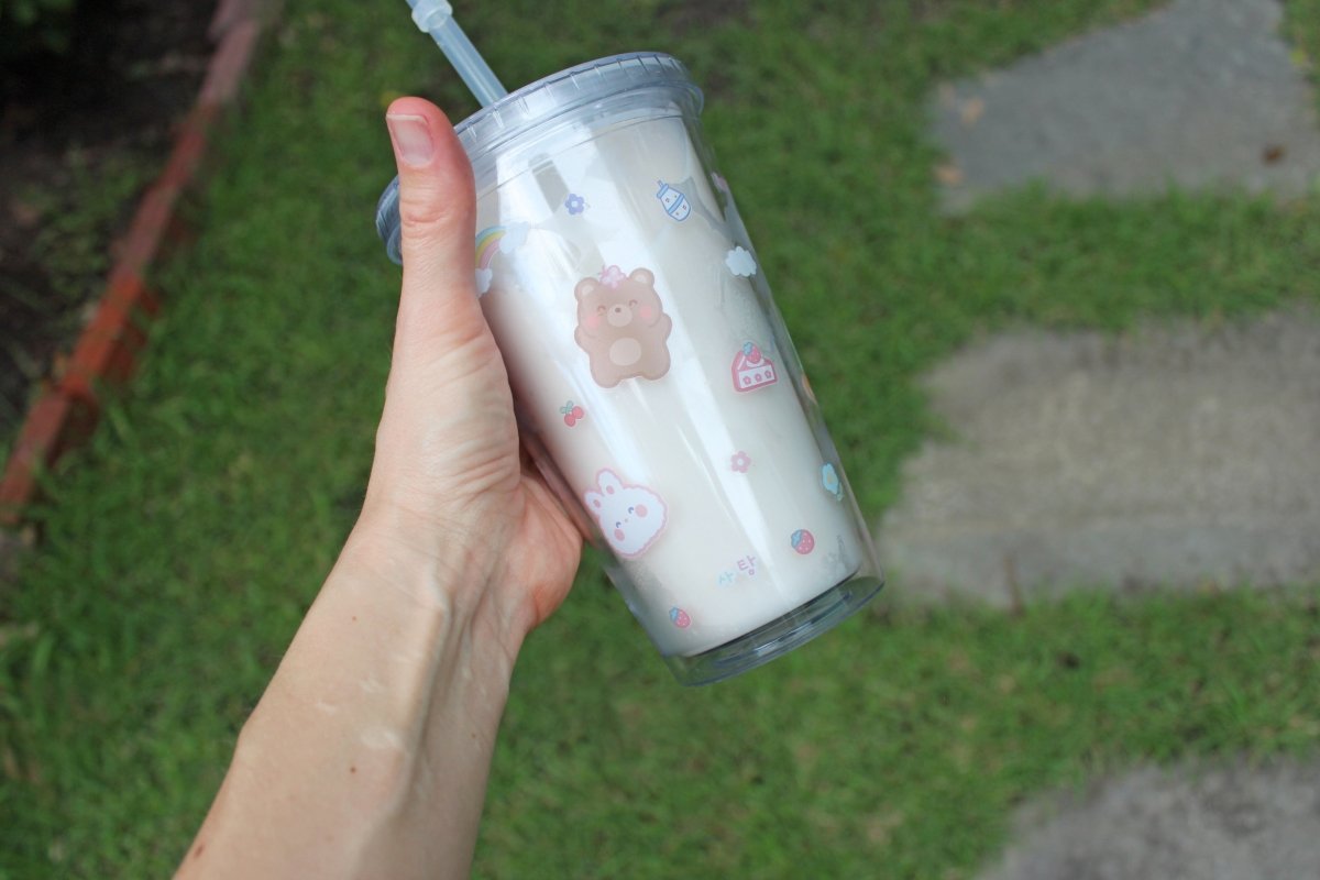 Someone holding up a kawaii 16oz tumbler cup to show off the pattern outdoors.