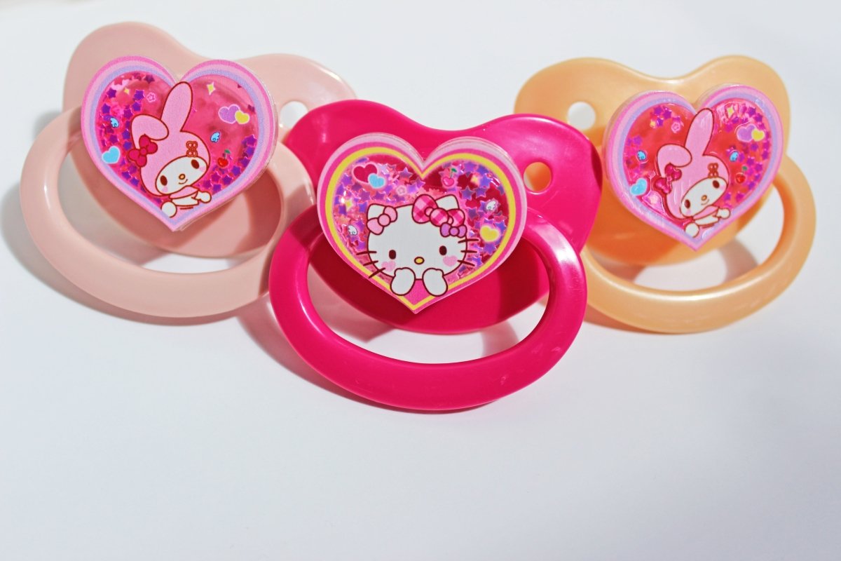 three shaker charm adult pacifiers lined up on a white background.