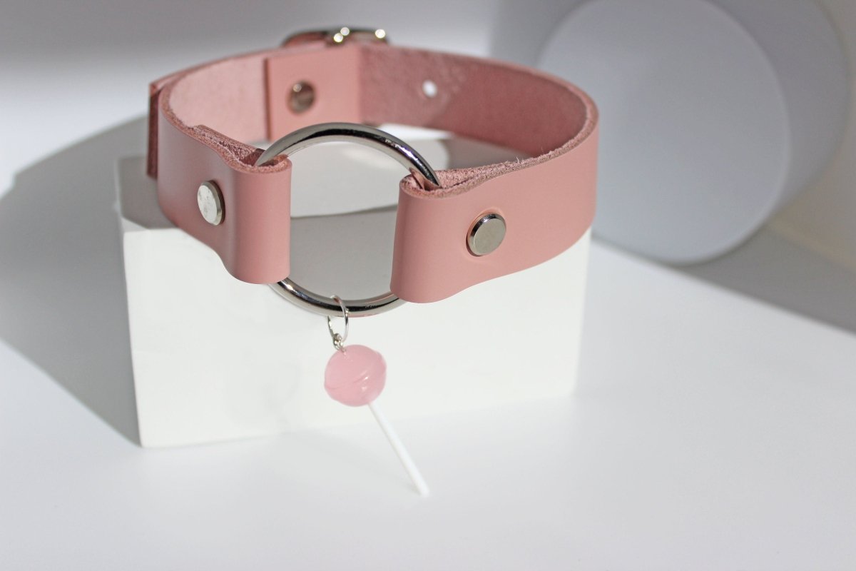 Pink leather lollipop submissive collar set on a white block on a white background.