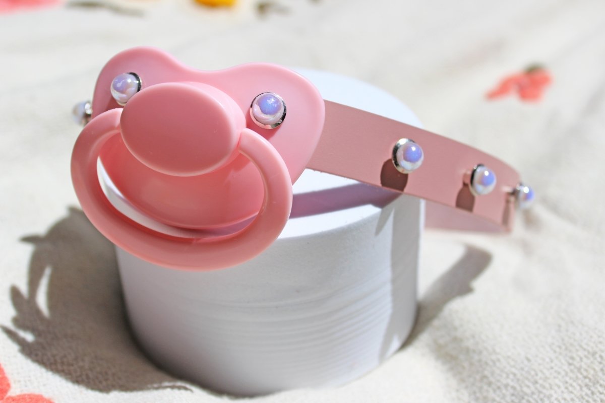 Pink pearl rivet adult pacifier gag placed on a white stand on a blanket.