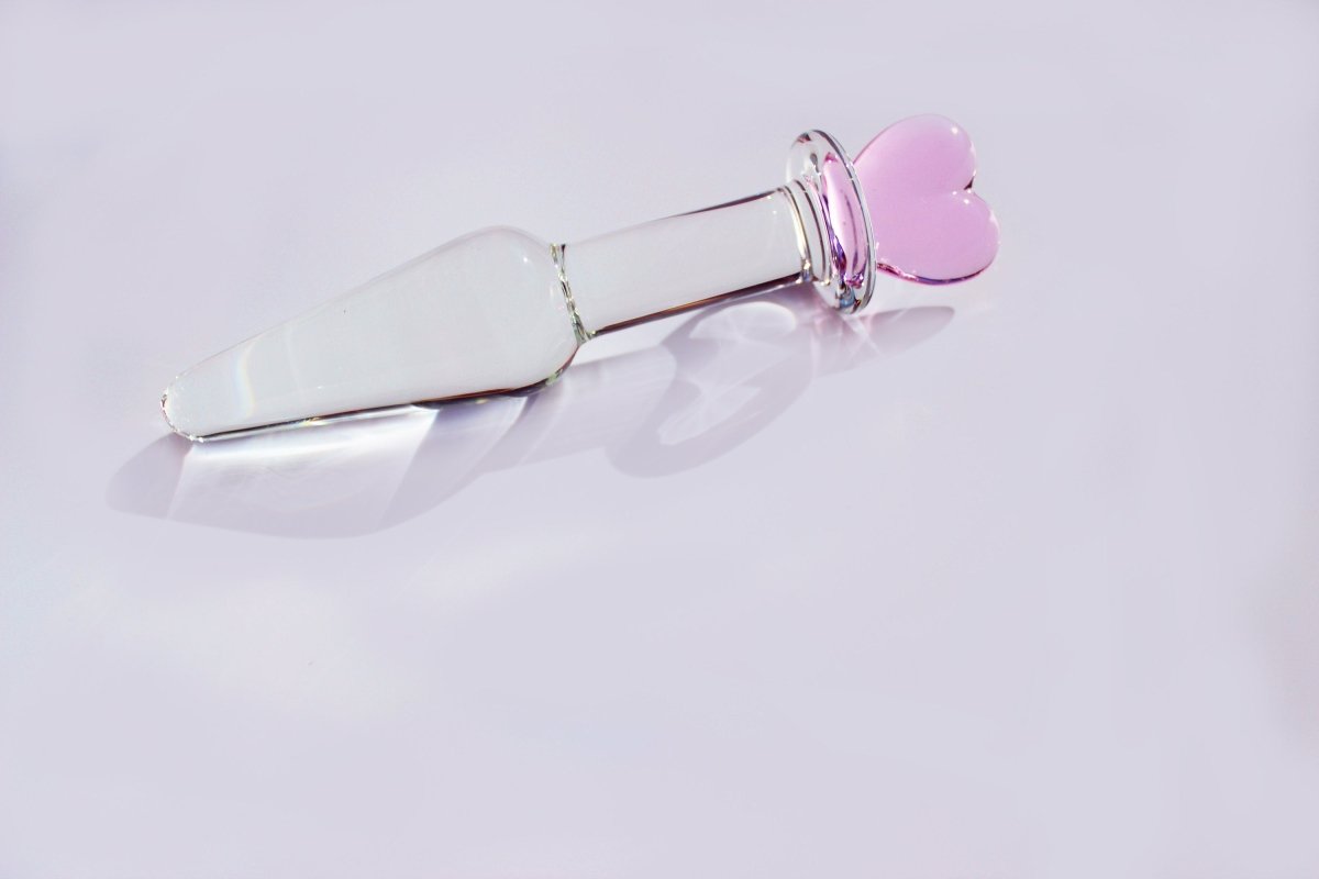 tapered clear glass butt plug with a pink heart base on a white background