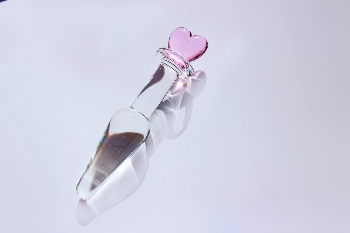 tapered clear glass butt plug with a pink heart base on a white background